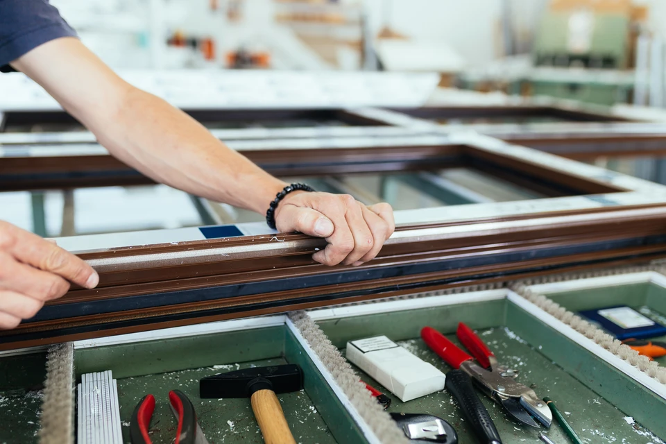 Atelier de menuiserie intérieur avec artisan manipulant des profilés de fenêtres en bois