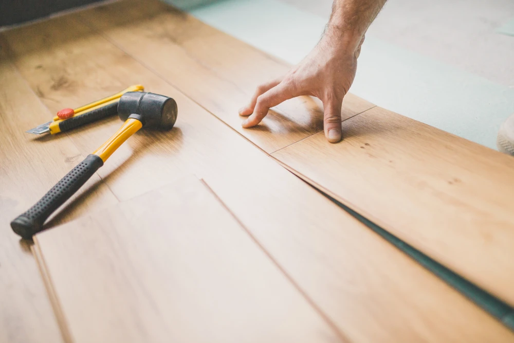 Ouvrier installant du parquet en bois clair dans un intérieur résidentiel, main positionnée sur une lame pour ajustement précis