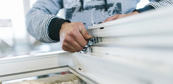 Int&eacute;rieur d'atelier, homme en chemise ray&eacute;e assemblant meuble blanc, manipulation pr&eacute;cise d'&eacute;l&eacute;ments de fixation m&eacute;talliques