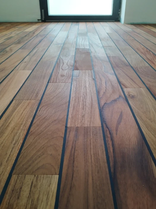 Parquet massif en bois exotique (ipé ou cumaru), pose en lames parallèles avec joints noirs au caulking souple, finition huilée ou vitrifiée satiné