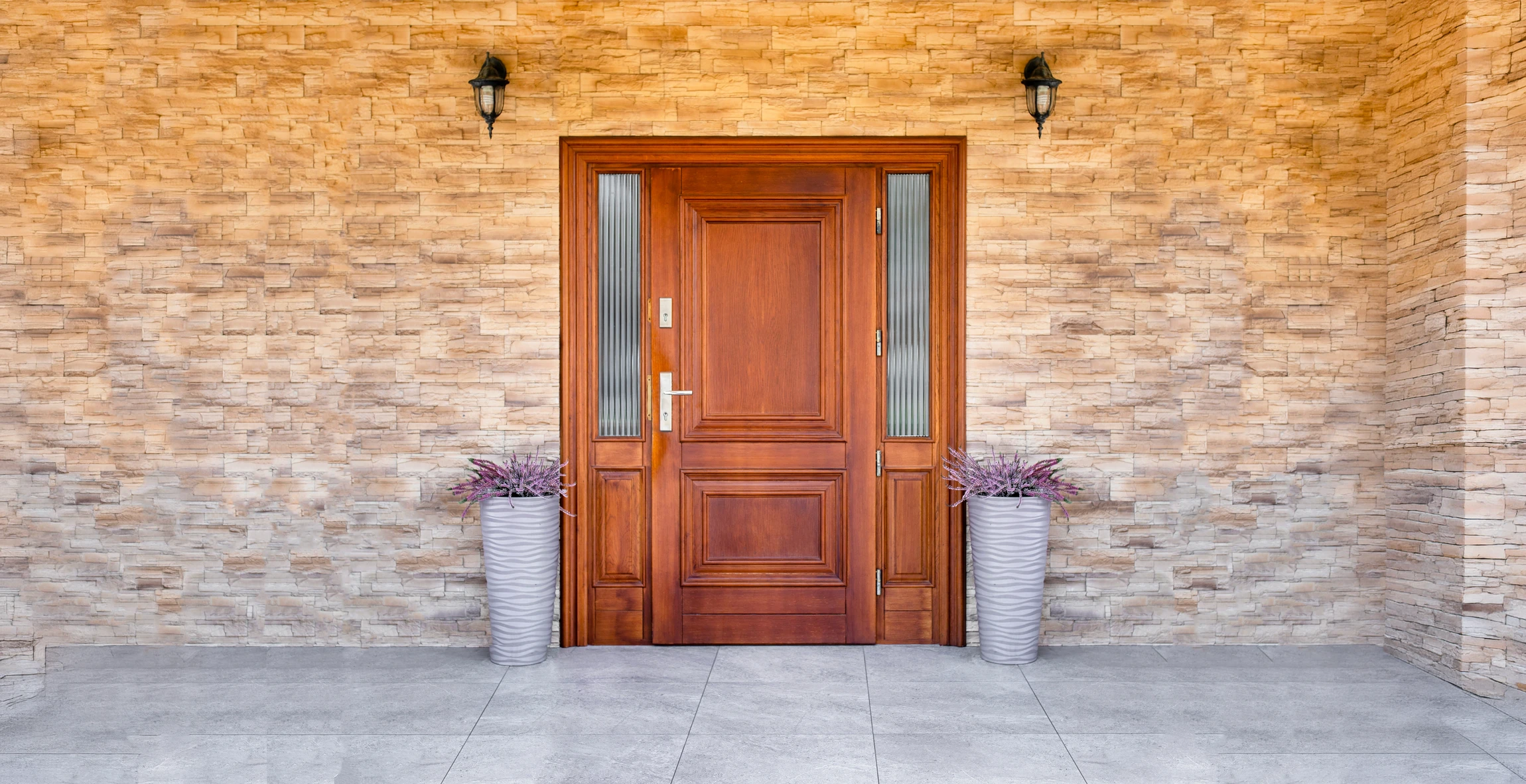 Entrée extérieure d'une maison résidentielle avec porte en bois clair ouverte sur jardin verdoyant et habitations en arrière-plan