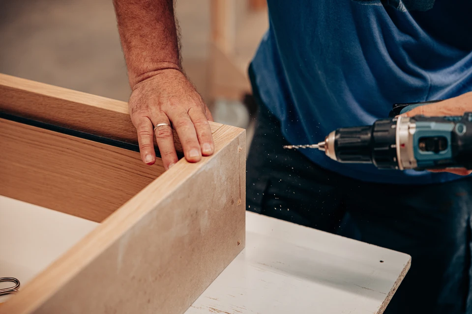 Un artisan menuisier en atelier travaillant sur la fabrication d'une porte ou d'une fenêtre en bois ou PVC, effectuant les finitions ou l'assemblage des éléments, avec outils professionnels visibles. L'accent doit être sur le savoir-faire artisanal, la précision du travail et la qualité de l'ouvrage en cours de réalisation.
