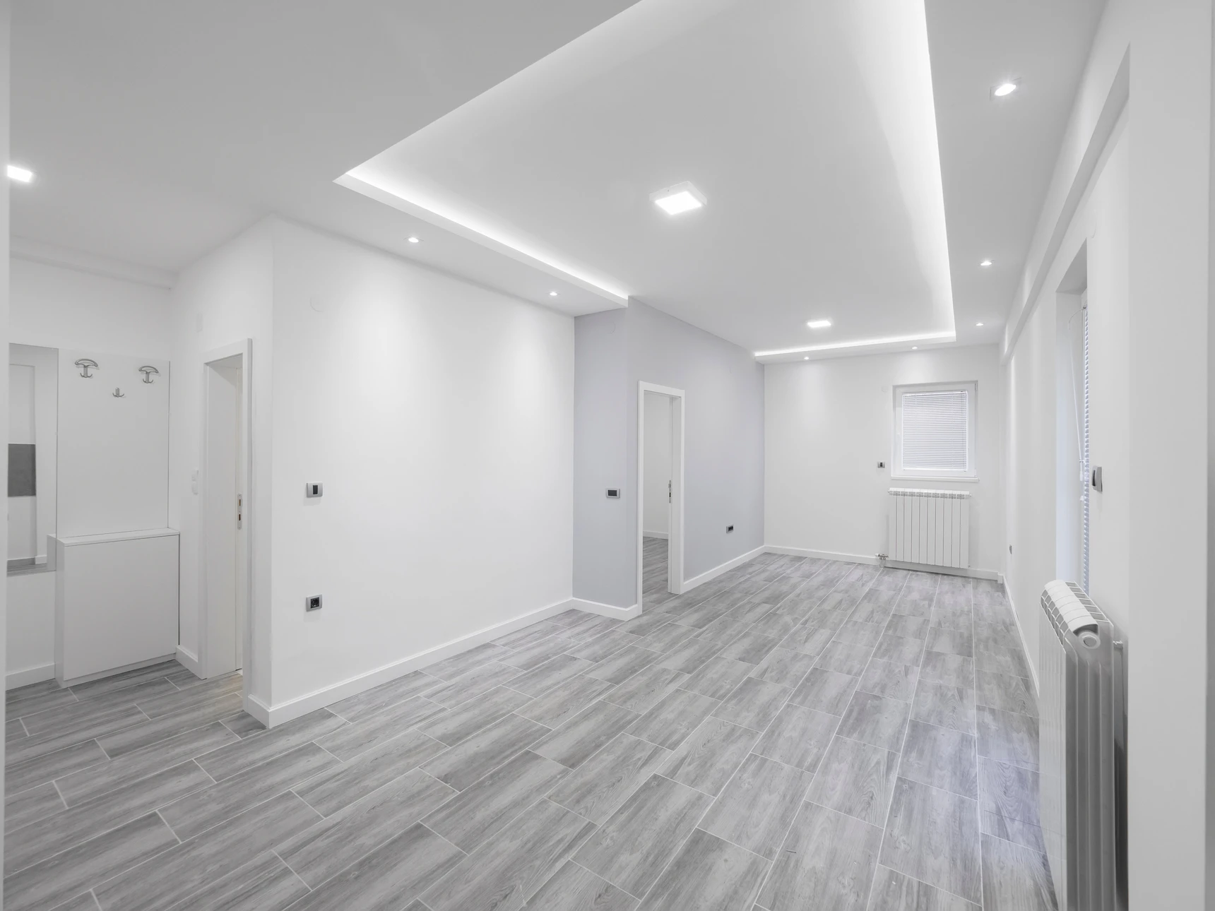 Intérieur résidentiel en cours de finition avec escalier en bois, murs en plaques de plâtre non peintes, grandes baies vitrées donnant sur terrasse